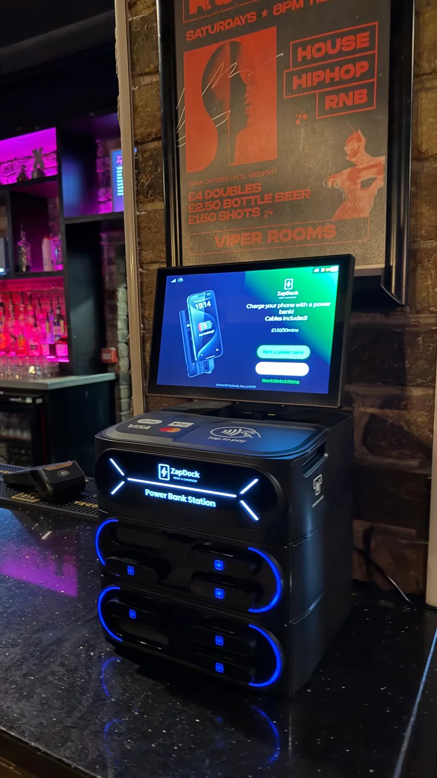 Blue illuminated ZapDock countertop station beside a purple-lit bar
